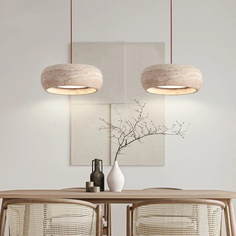 A minimalist dining area showcases Morsale's modern travertine pendant lights, a wooden table with woven chairs, and a white vase with branches. Neutral wall art completes the serene ambiance.