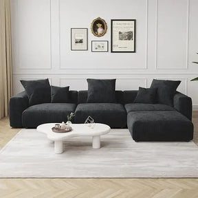 A contemporary living room features a Morsale Corduroy Modern Sectional Couch Sofa on a light rug, alongside an oval white coffee table with decor. Framed art adorns the walls, while the light wood floor enhances the minimalist style.