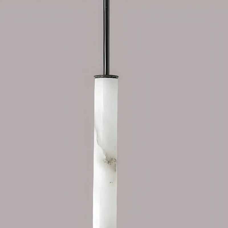 The Natural Marble & Brass Pendant Light Fixture from Morsale.com showcases a long, cylindrical white shade with a natural marble pattern, suspended from a sleek black rod. The polished brass finish adds an elegant touch, beautifully contrasted against a plain gray background.