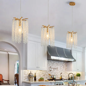 A modern kitchen showcases Morsale's Albero Crystal Pendant Lights, Set Of 3, elegantly hanging from the ceiling. It features white cabinetry, a stainless steel range hood, and a countertop adorned with various kitchen essentials and wine bottles.