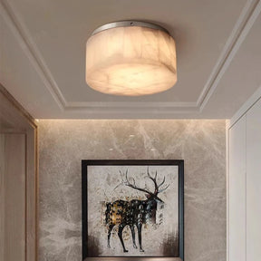 The Moonshade Natural Marble Ceiling Light Fixture from Morsale.com, featuring a frosted glass shade and energy-efficient LED lights, is installed in a room with beige marble walls. Below it, a framed painting of a deer hangs on the wall, and a slim console table with a decorative piece is placed beneath the painting.