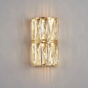 The Bacci Crystal Wall Lights from Morsale.com feature a modern, rectangular, transparent glass design that emits a warm white light. Adorned with handmade crystals arranged in a geometric pattern, these wall sconces are mounted on a plain white wall to create a soft ambiance.