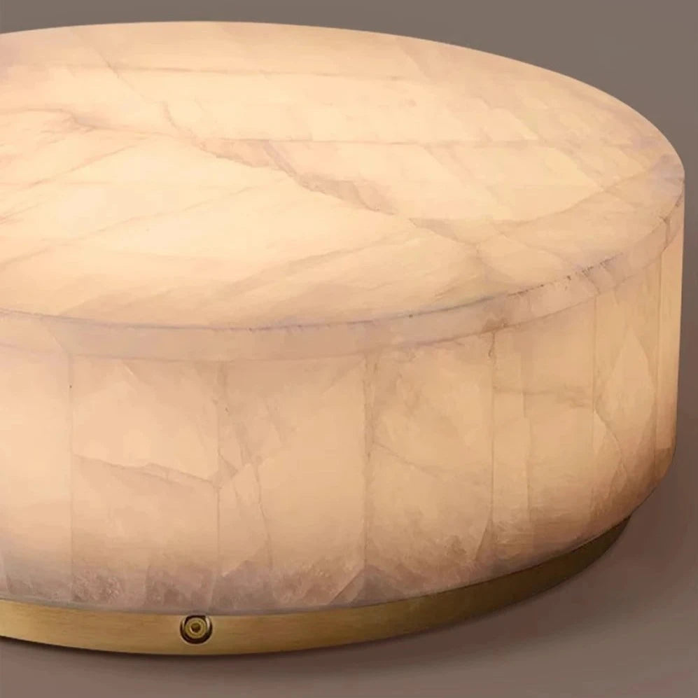 The Moonshade Natural Marble Ceiling Light Fixture by Morsale.com features a polished finish with a smooth, light-colored surface that mimics natural marble. It is supported by a brass base and emits a soft, warm glow from energy-efficient LED lights within, highlighting its translucent stone texture against a plain gray background.