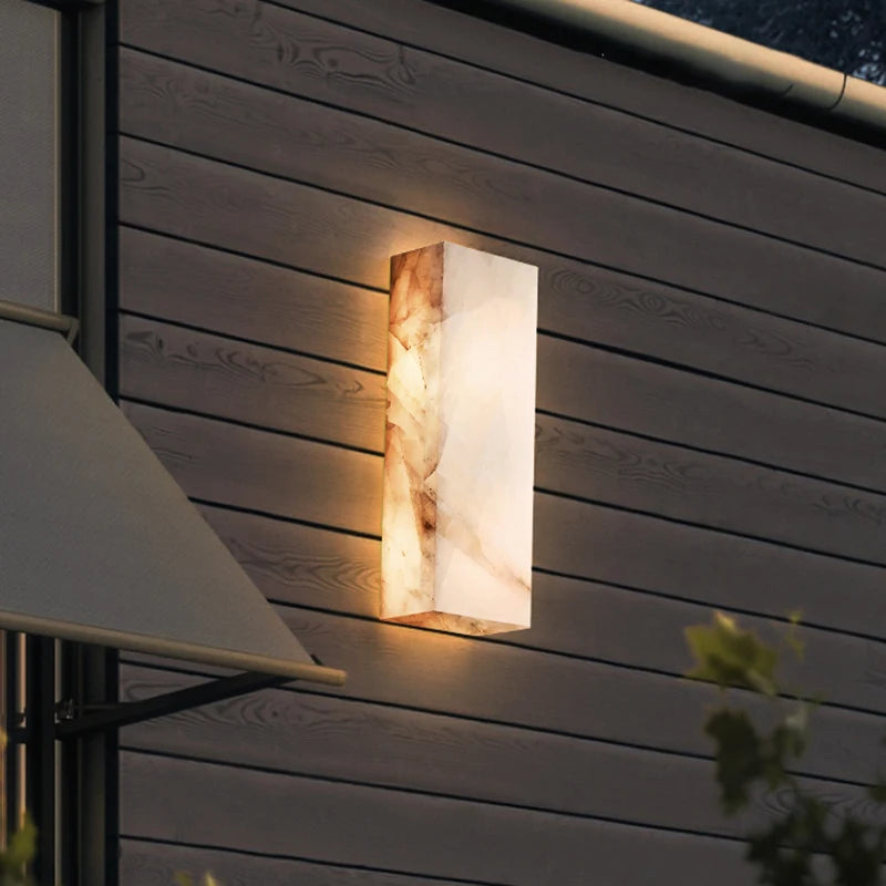 
                  
                    The Morsale Outdoor Marble LED Wall Lamp (IP65 Waterproof) casts a warm glow on horizontal wooden siding at dusk, with green leaves and part of a canopy visible in the foreground.
                  
                