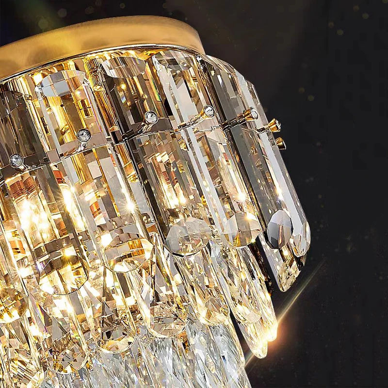 A close-up shot of the luxurious Morsale.com Giano Ceiling Light Fixture lit up, showcasing its intricate design with multiple handmade crystal prisms hanging elegantly from a golden frame against a dark background. The light reflecting off the crystals creates a dazzling effect.