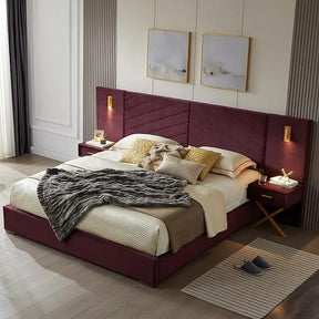 A bedroom features a Morsale King Size Bed with lighting and bedside tables, showcasing a velvet upholstered burgundy headboard. Cream, beige, and gray bedding is complemented by a textured throw. Two abstract paintings hang above, with wall-mounted lights illuminating the scene. Nearby rest slippers.