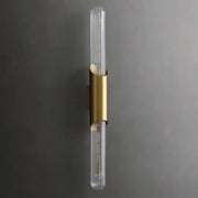 An elegant lighting solution, the Palermo 23" Brass Wall Sconce Light by Morsale features a vertical cylindrical glass design. Mounted on a wall, it showcases brass accents dividing the two transparent tubular bulbs, creating a modern and sophisticated appearance against a dark background.