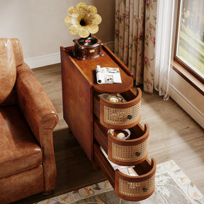 The Morsale Irvine Solid Wood Side Table with a vintage finish is beside a leather couch, topped with a gramophone and rolled papers. Inside the sliding drawers are a book and pocket watch. A curtain-draped window behind offers a charming garden view.