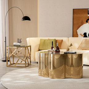 A modern living room showcases a cream sofa, gold accent pillows, and a Morsale Stainless Steel Gold Coffee Table. A geometric side table and curved floor lamp enhance the style, while large abstract artwork adorns the wall. The soft natural light creates an inviting ambiance.