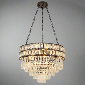 The Gio Modern Crystal Chandelier by Morsale showcases an elegant and modern style with multiple tiers of hanging glass prisms suspended by metal chains. This stunning chain pendant casts a warm glow, accentuating its intricate design against a gray backdrop.