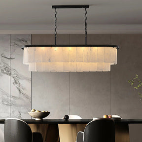 A modern dining room showcases Morsale’s elegant Moonshade Marble Chandelier, featuring layered translucent panels and a natural marble shade. Below, a sleek table displays a bowl of fruit and décor. Moonshade Marble walls complete the sophisticated ambiance.