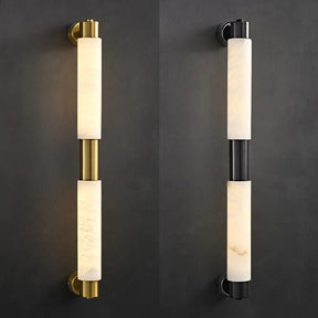 Mounted on a dark wall are two wall sconces: the left sconce showcases a sleek design with a brass finish, while the right one is an elegant Morsale Moonshade Natural Marble Wall Lamp in matte black. Both feature cylindrical cream-colored shades that offer a diffused light effect.