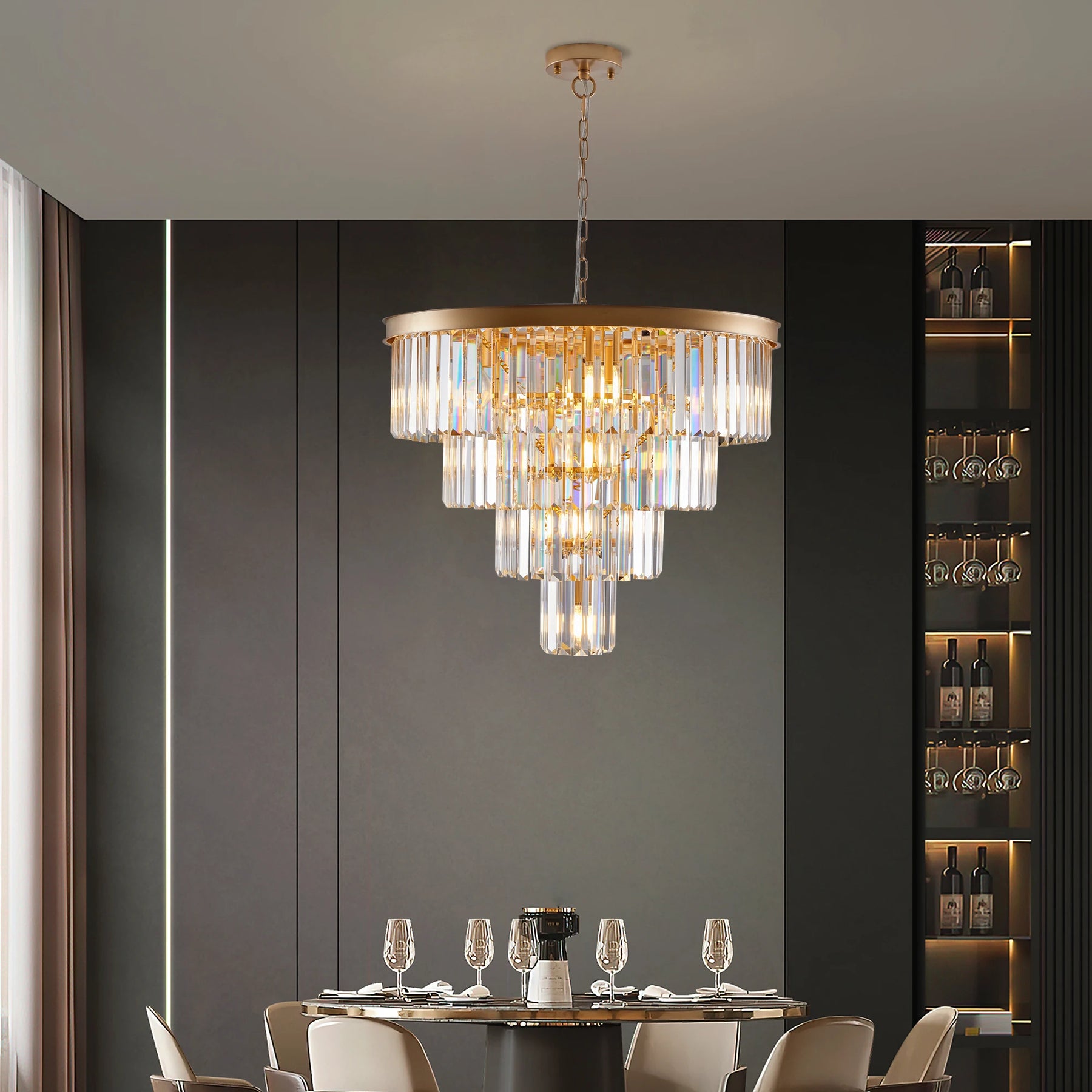 A contemporary dining room showcases a round table set with wine glasses and decor. Hanging overhead is the Morsale 23.6" Gio Crystal Chandelier, featuring cascading glass prisms. In the background, a shelf displays wine bottles.