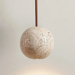 The Travertine Ball Pendant Light Fixture from Morsale.com, crafted from natural travertine stone, features a beige, porous surface that exudes a rustic and organic charm as it hangs from the ceiling. This elegant light fixture is suspended by a brown cord against a plain, off-white background.