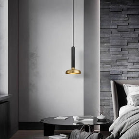 A modern bedroom showcases a dark gray stone accent wall and the sleek All Copper Modern Pendant Light by Morsale, illuminating the room with warm LED bulbs. A round black coffee table complements the stylish decor, while a window on the left floods the space with natural light.