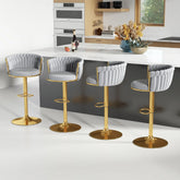 Four Morsale Height Adjustable Counter Stools with gold bases and gray quilted upholstery, featuring a 360° swivel, line up at a kitchen island. The kitchen has light wood cabinets, a white counter, built-in ovens, and a window adorned with a wine bottle and flower arrangement.