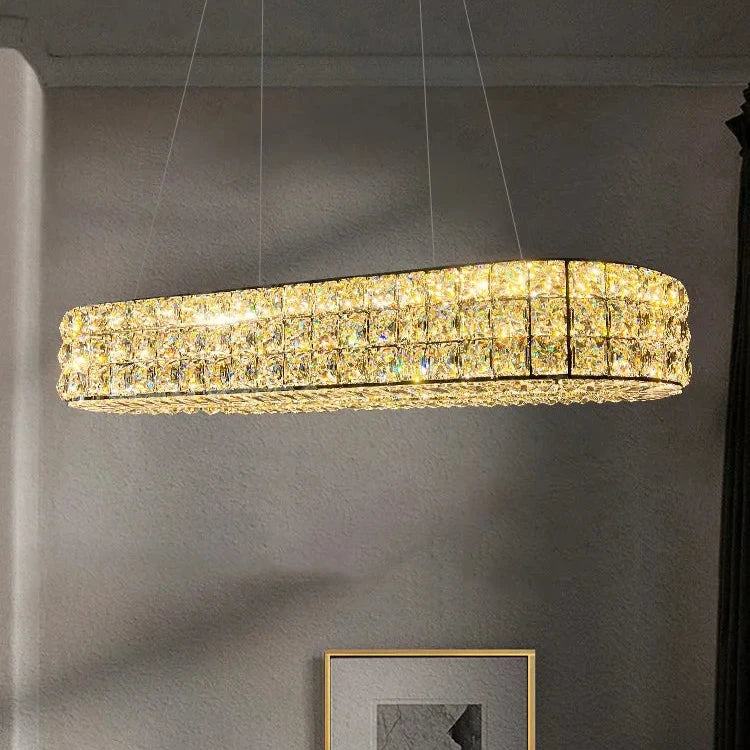 The minimalist room features a Bacci Crystal Dining Room Light Fixture from Morsale. This rectangular, modern chandelier emits a warm glow as it hangs above a wall displaying a framed black and white picture against light-colored walls.