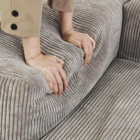 A close-up shows a person pressing hands into the cushion of a Morsale Corduroy Modern Sectional Couch Sofa, demonstrating its softness and flexibility. They wear a beige jacket with buttoned sleeves, highlighting this stylish living room piece.