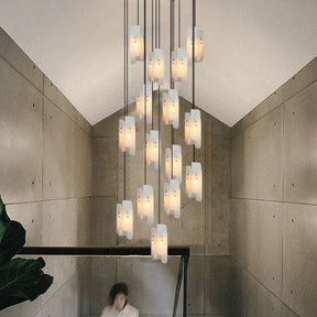 A stunning arrangement of Moonshade Natural Marble Pendant Lights by Morsale illuminates a high-ceilinged room with concrete walls. A person is partially visible descending a staircase in the lower left corner, enhancing the ambiance of luxury lighting.