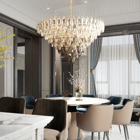 The elegant dining room is graced by the Lazzo Contemporary Chandelier from Morsale, which is adorned with LED bulbs and suspended above a round white dining table surrounded by cushioned chairs. The space is characterized by tall windows draped in sheer curtains and a vase filled with branches, contributing to its modern and sophisticated ambiance.