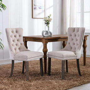 A set of Morsale Velvet Tufted Dining Chairs in beige with nailhead trim complements the wooden table, exuding a minimalist modern vibe. A sleek vase with white flowers sits on a brown shaggy rug, while framed art and a bright window enhance the serene atmosphere.