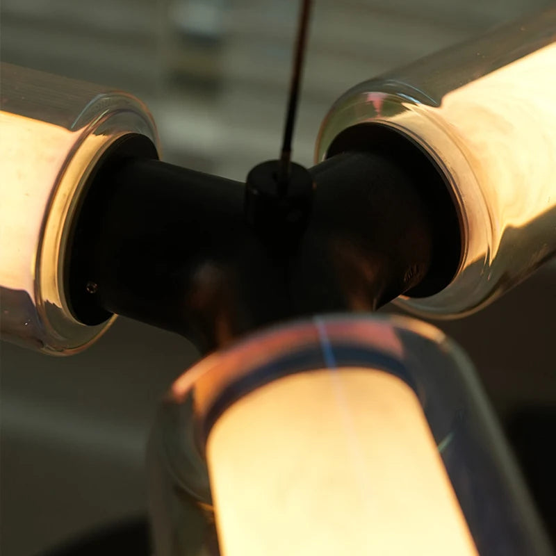 
                  
                    Close-up of the Morsale Lumière Pendant Marble & Glass Suspended Light, featuring three glowing tubular bulbs joined at a central black fixture. The warm light contrasts elegantly with the modern dark design.
                  
                