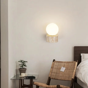 The Modern LED Travertine Wall Sconce from Morsale.com features a travertine base with natural beige and light brown patterns, topped with a large, smooth frosted globe light. Equipped with LED bulbs, the globe emits a soft, warm glow that casts gentle light on the wall.