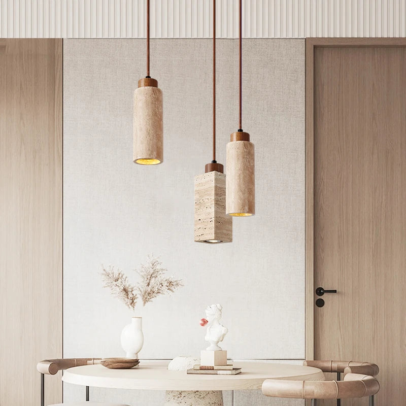 Three Natural Travertine Pendant Lights from Morsale.com with cylindrical beige shades hang from the ceiling. The central light, elegantly crafted from travertine, showcases a square, stone-like shade, while the two on either side feature round, smooth shades. All lights include LED bulbs and matching brown cords for a cohesive look.