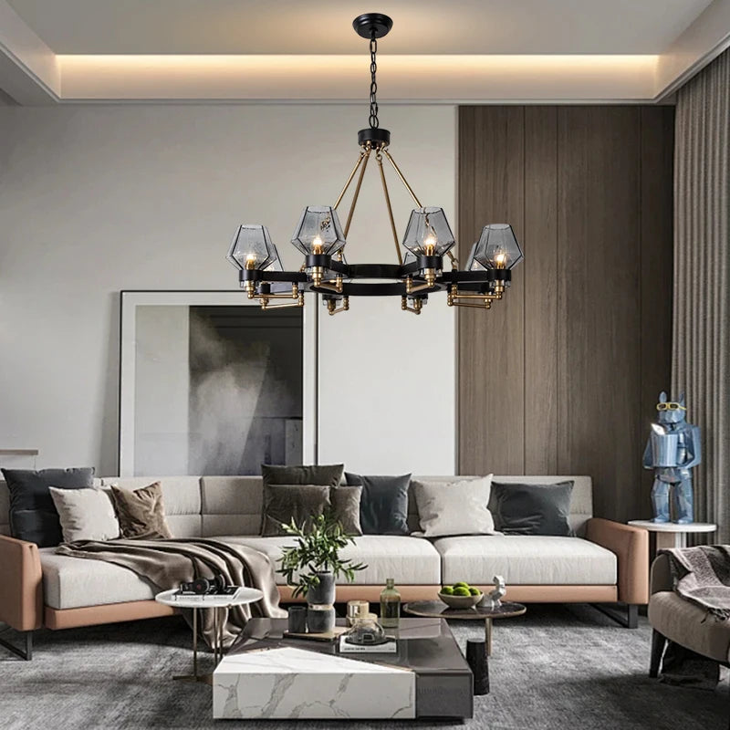 A modern living room features a sleek Retro American Pendant Chandelier Light Fixture by Morsale.com with six geometric glass shades hanging from the ceiling. The room includes a large sectional sofa with cushions, a marble coffee table adorned with plants, and contemporary artwork on the back wall.