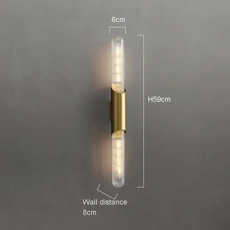 A Palermo 23" Brass Wall Sconce Light by Morsale, featuring two ribbed glass light tubes extending vertically from the center. The elegant lighting fixture stands 59 cm high, 6 cm wide, and protrudes 8 cm from the plain gray wall.