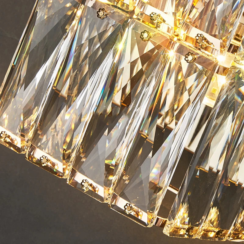 Close-up of a Bacci Crystal Wall Sconce by Morsale, featuring triangular crystal prisms hanging vertically that reflect warm LED light. These prisms create a sparkling effect with hints of color against a dark backdrop, enhancing the modern style.