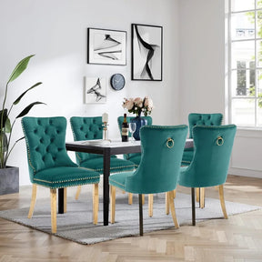 A modern dining room features a white-topped rectangular table with six Morsale Tufted Dining Chairs in teal, gold legs contrasted against light wood flooring. Walls are adorned with solid wood artwork, a clock, and a plant; a bouquet and wine bottles add to the scene.