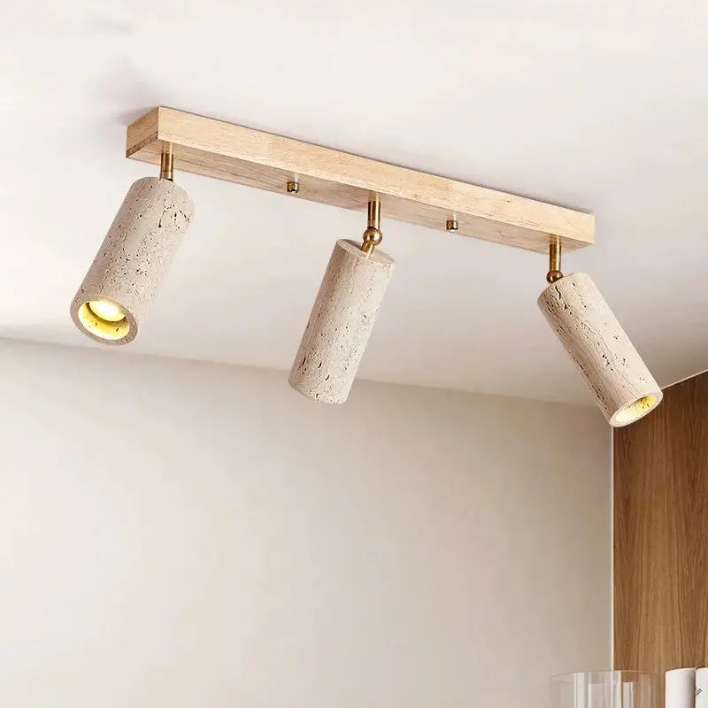 The 3-Head Natural Travertine & Wood Spot Light Fixture by Morsale.com features three adjustable LED spotlights mounted on a wooden ceiling panel. With their efficient LED bulbs and textured travertine finish, the spotlights emit a warm glow. The letters "GYS" are displayed in the top left corner of the image.