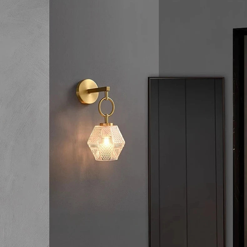 A contemporary interior showcases the Morsale Copper & Glass Pendant Wall Sconce, featuring a hexagonal design with a textured glass shade that emits warm light from energy-efficient LED bulbs. The gray wall is enhanced by a full-length mirror and a patterned bench, contributing to the chic ambiance.