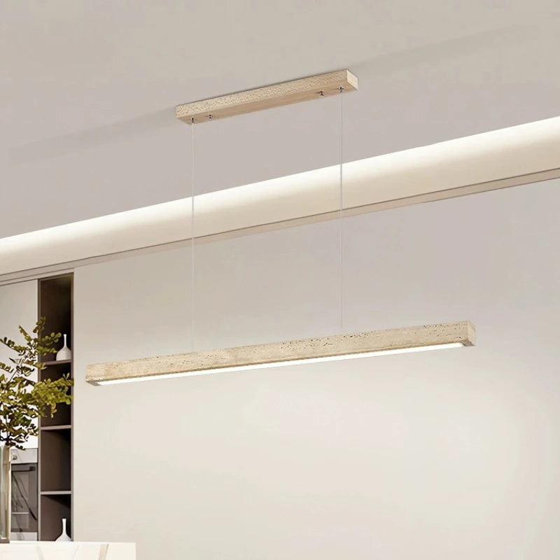 A minimalist, modern cord pendant light fixture from Morsale.com hangs from a high ceiling in a stylish, contemporary room. The Natural Travertine LED Kitchen Light Fixture features a long, rectangular wooden beam with LED bulbs suspended by two thin, nearly invisible cables. The room has clean lines and subtle beige tones.