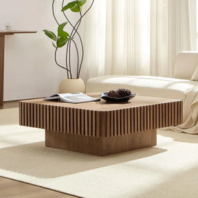 A stylish living room displays the Morsale Belford Walnut Coffee Table, featuring vertical grooves, with an open book and decorative item on top. A white sofa and potted plant sit in the modern setting as natural light filters through sheer curtains.