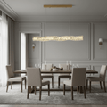 Bacci Modern Linear Crystal Dining Room Chandelier elegantly illuminating a stylish dining room with wooden table and beige chairs.