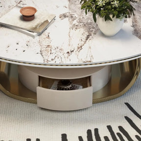 The Morsale 55" Modern Cocktail Table with Storage features a round marble design and a small open drawer showing a decorative piece. A potted plant and brown dish adorn the table, resting on a stylish patterned rug.