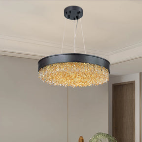 The Alleri Modern Chandelier by Morsale, with its sleek black frame and circular design, hangs elegantly from the ceiling. It is adorned with cascading golden crystal-like embellishments that provide a warm LED glow, brightening the room's neutral-toned walls and decor and accentuating its contemporary style.