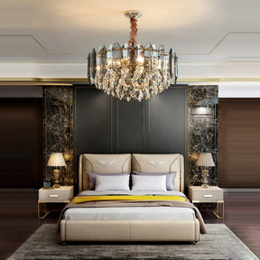 Luxurious bedroom featuring the Morsale Lazzo Modern Chandelier, elegantly illuminated with LED bulbs. The room includes a bed with a beige headboard adorned with decorative pillows and a yellow blanket, complemented by two bedside tables each topped with lamps. The space is characterized by dark marble walls and contemporary modern decor.