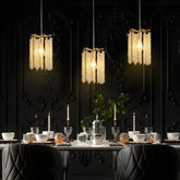 A dimly lit dining room showcases a table with elegant dishware and lit candles. Three Albero Crystal Pendant Lights by Morsale hang above, casting a warm glow on a dark, intricately designed wall, blending modern style with classic elegance.