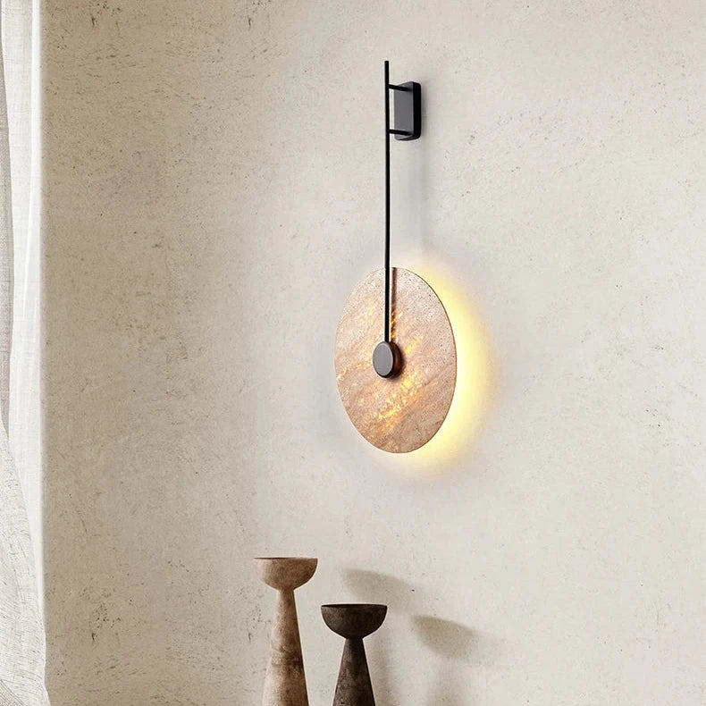 Moonshade Natural Marble Sconce by Morsale is a wall-mounted circular light fixture with a minimalistic design and thin black support. Below, three decorative goblets in varying heights and shades create a striking display against the light-colored wall, perfectly complementing the sleek aesthetic of the sconce.