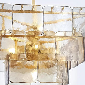 A close-up of the Welle Glass Chandelier by Morsale showcases layered, rectangular glass panels with a textured finish. LED bulbs illuminate the chandelier, producing a warm, glowing effect that highlights its golden metal accents. The touch on/off switch adds modern convenience to this Art Deco-inspired lighting piece.