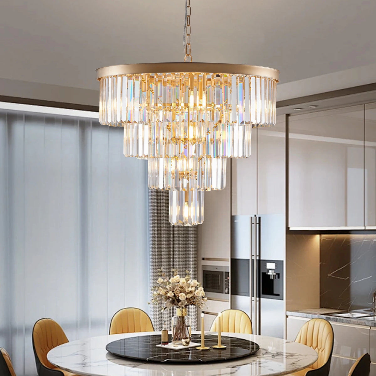 A dining room with the Morsale 23.6" Gio Crystal Chandelier, featuring multiple tiers of cylindrical crystals. Below it, a round table is adorned with a floral centerpiece and candles. The room includes beige chairs and has floor-to-ceiling windows as the backdrop.