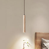 A sleek, cylindrical pendant light from Morsale.com, the Natural Travertine Modern Pendant Light, hangs from the ceiling, casting a warm glow over a small potted plant. The background features a beige wall and a piece of wooden furniture with a light-colored cushion. The scene exudes a minimalist, cozy ambiance.