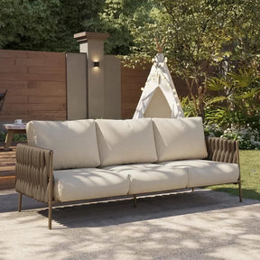 The Morsale Kington Waterproof Outdoor Sofa in beige elevates the patio, nestled among lush greenery and trees. Accompanied by a wooden fence and a decorative teepee with string lights, it requires no assembly to create the perfect retreat.