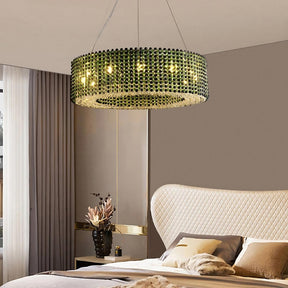 A modern bedroom showcases an Alleri Crystal Beads Luxury Chandelier by Morsale.com, adorned with black, green, and clear crystals. The room features a beige quilted headboard, neutral bedding, a gold-accented wall, and a vase with flowers near the window.