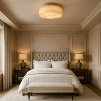 A stylish bedroom with a large tufted bed, white bedding, cushioned bench, matching bedside tables with lamps, and soft beige walls is illuminated by the elegant Milton Marble Flush Mount from Morsale.com.
