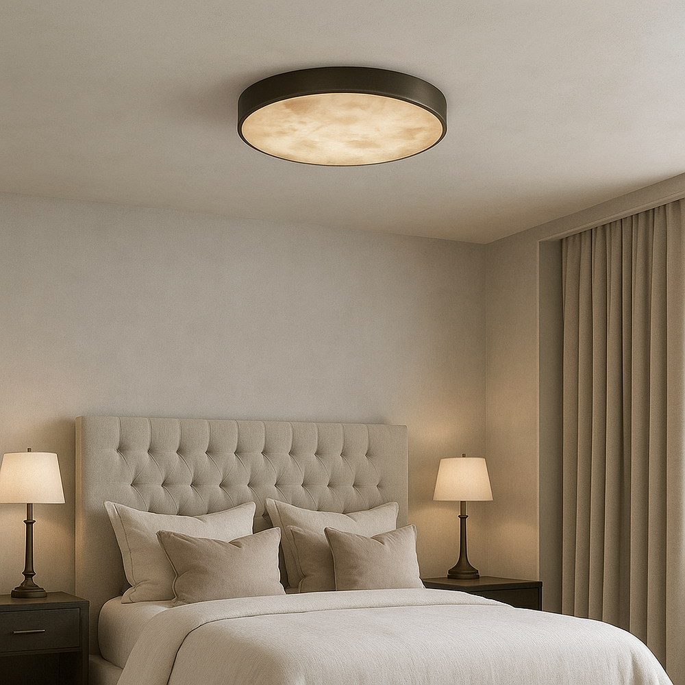 A modern bedroom featuring a large tufted headboard, neutral bedding, two bedside tables with lamps, beige walls, floor-length curtains, and a minimalist Morsale Laurel Marble Flush Mount ceiling light.