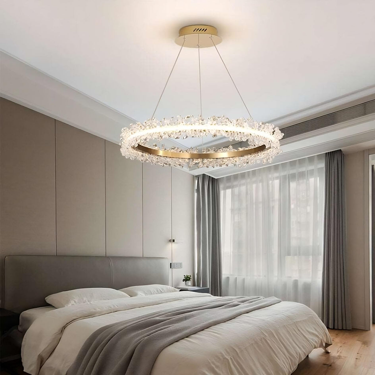 A modern bedroom with a large bed featuring white bedding and a gray headboard. A Capri Crystal Ceiling Light from Morsale.com hangs elegantly from the ceiling. The room has floor-to-ceiling windows with light gray curtains and beige walls, creating a serene ambiance.